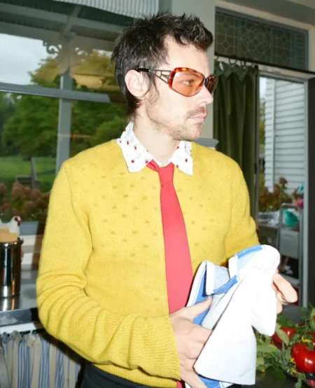 Harry Styles ripreso di profilo indossa una maglia gialla e cravatta rossa