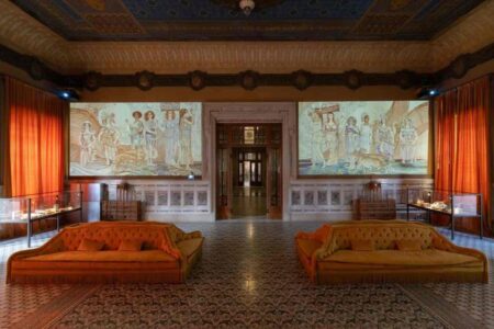 Due schermi con l'installazione di Dotdotdot in un'ampia sala con divani